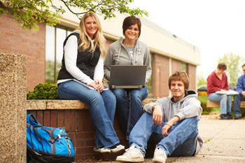 Three students seen seated outside of Red Wing campus, laptop open on lap of middle student